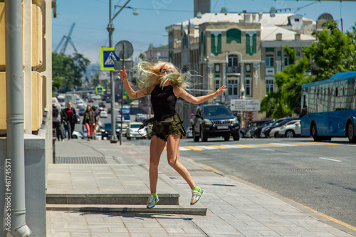 A young girl in glasses and khaki shorts is bouncing in the street along the road. A happy blonde.