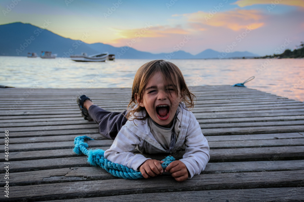 Portrait of a little boy screaming in amusement lying on a dock. Portrait of a little boy screaming in amusement lying on a dock.