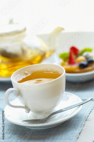 A cup of herbal tea with teapot and tart dessert on blue linen tablecloth. selective focus .