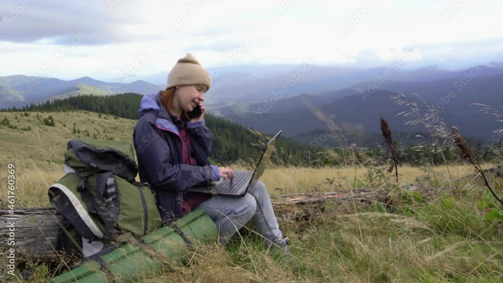 A young woman freelancer sits on a mountain top with a laptop and takes an order on her smartphone. Remote work anywhere in the world. A young woman freelancer sits on a mountain top with a laptop and takes an order on her smartphone. Remote work anywhere in the world.