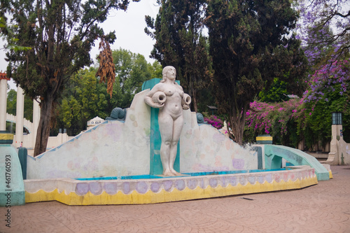 Statue of naked woman on fountain with tall trees as background