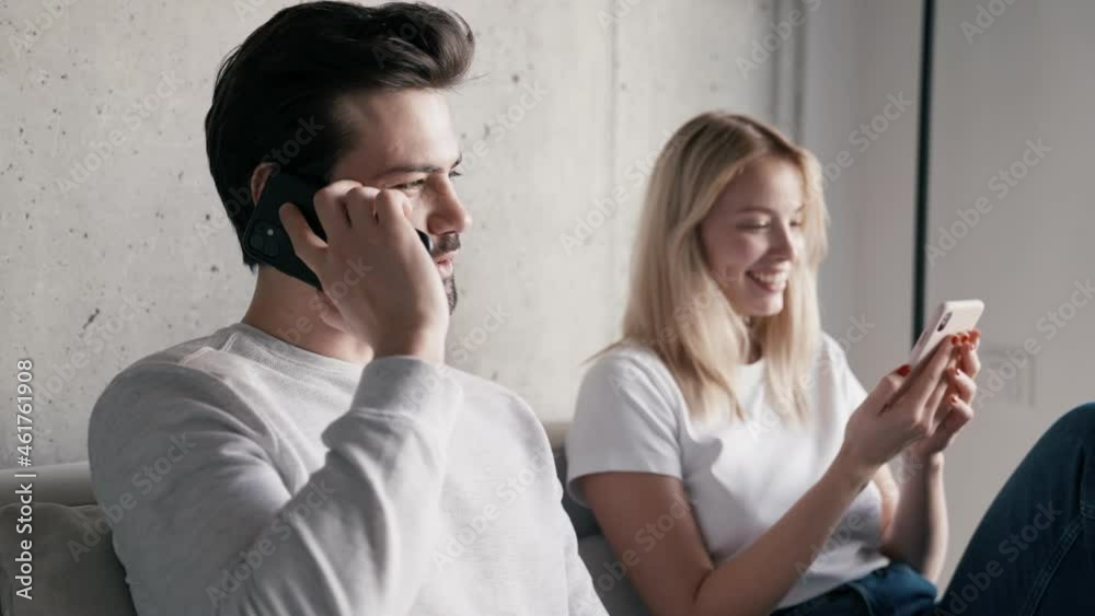 Positive man talking on the phone while his girlfriend leafing tape on the phone Positive man talking on the phone while his girlfriend leafing tape on the phone