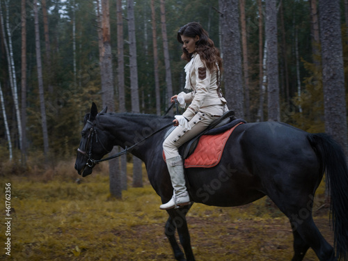 A young beautiful brunette rider in an elegant retro suit riding a black horse