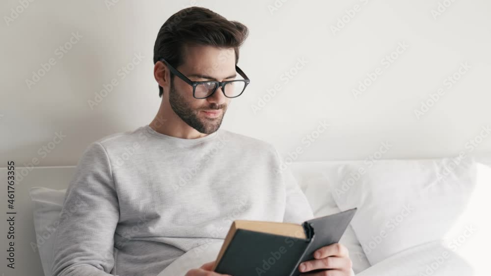 Concentrated man in eyeglasses reading book while lying on the bed Concentrated man in eyeglasses reading book while lying on the bed