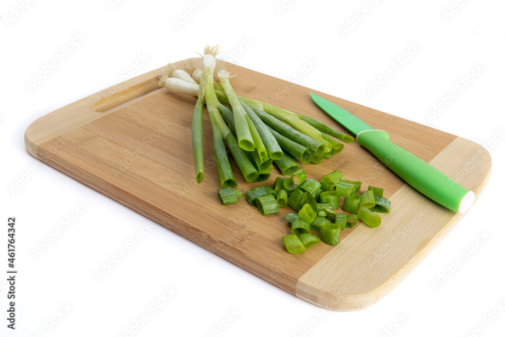 A bunch of green onions or shallots on a wooden cutting board with a green paring knife with pieces cut off A bunch of green onions or shallots on a wooden cutting board with a green paring knife with pieces cut off