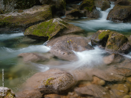 small river deep in the green woods. wonderful springtime scenery of mountains countryside. clear water among forest and rocky shore. wooden fence on the river bank.