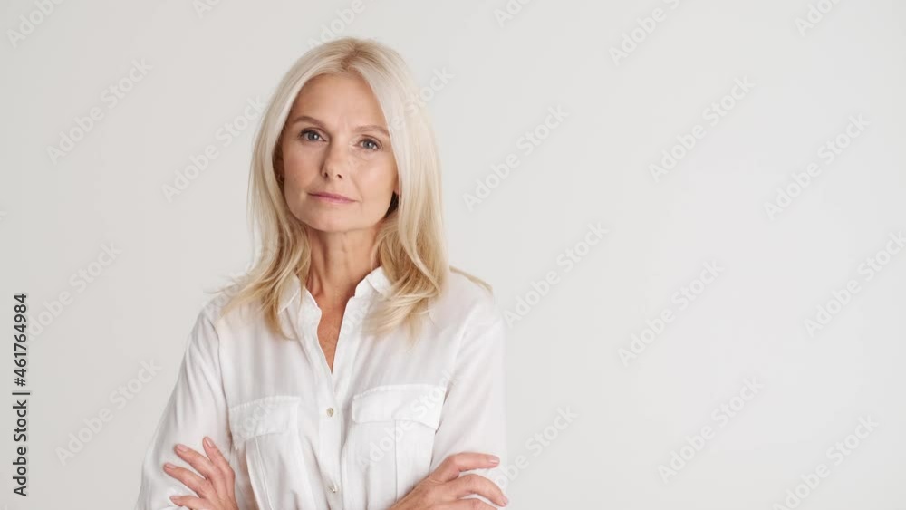 Serious mature woman holding hands and looking at the camera in the white studio Serious mature woman holding hands and looking at the camera in the white studio