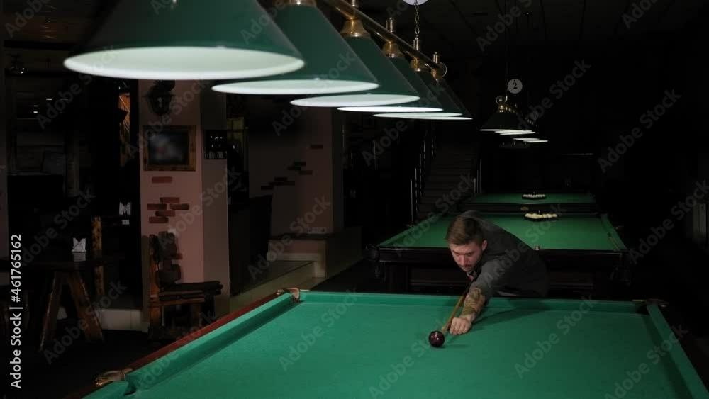 Closeup of a man playing pool in a dark bar, he takes aim and prepares