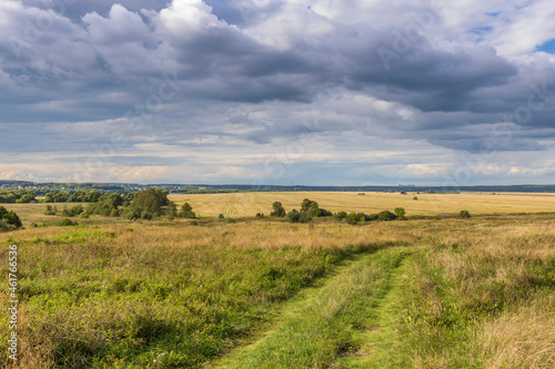 Road through fields. Country road in summer field and clouds on blue sky.