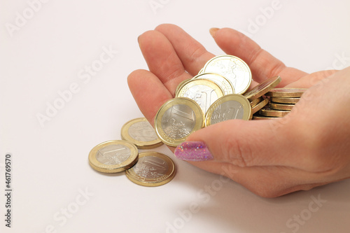 Caucasian white female hand with manicured nails and pink glitter nail polish holding and pouring a couple of new 1 Euro coins reverse (number side on top). Isolated on white background. photo