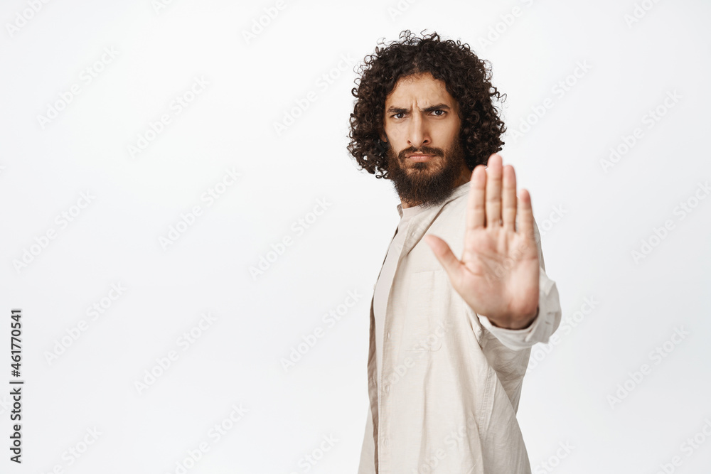 Serious and confident middle-eastern man extend arm, stop sign, say no, disapprove and prohibit smth, rejecting, standing over white background Serious and confident middle-eastern man extend arm, stop sign, say no, disapprove and prohibit smth, rejecting, standing over white background