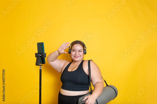 plus size model with sportswear waving to the mobile phone in online sports class to lose weight photo