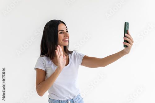 Happy young woman making selfie photo while waving palm on a white background