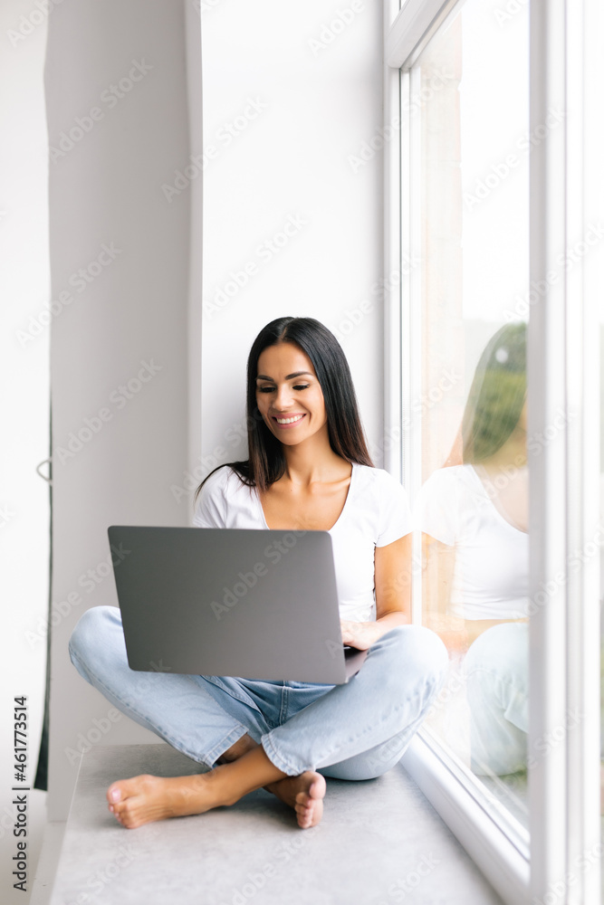 Young woman with a laptop on the windowsill Young woman with a laptop on the windowsill