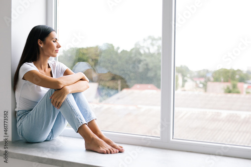 Sad depressed woman having social problems sitting on windowsill