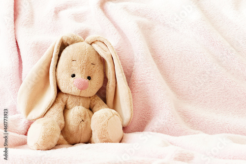 Children's background with a bunny toy. A soft, stuffed rabbit on a pink blanket. Concept for baby design.