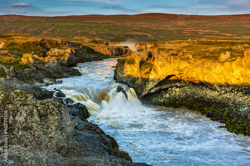 dramatic sky during sunrise illuminating the powerful Godifoss waterfall in Iceland.