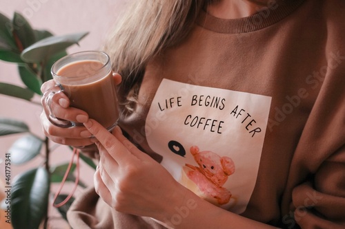 A cute beautiful young woman with a cup of coffee. Life begins after coffee is written on the sweatshirt. Drinking coffee with milk.