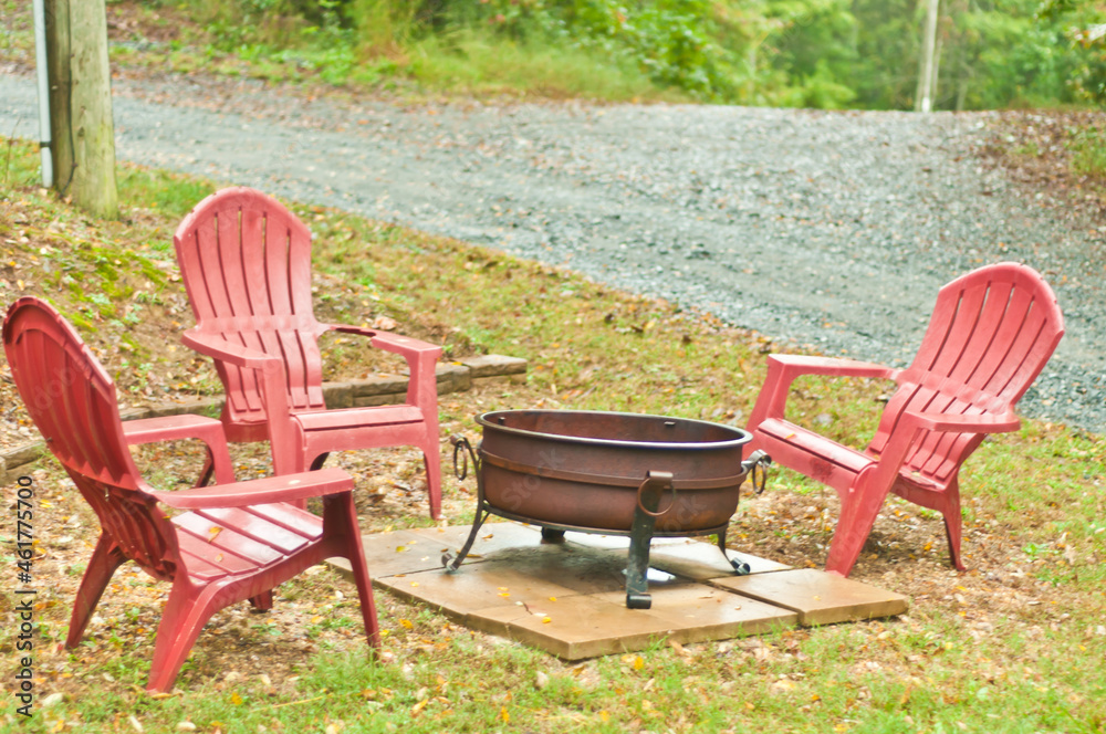 front view, medium distance of a metal, fire pot with three red Adirondack chairs, in front of a cabin in the blue ridge mountains in autumn