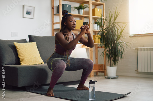 Fotografía Happy African American sportswoman exercises squats with power band around her legs during home workout