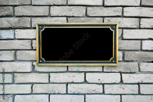 Black commemorative plaque in golden frame fixed on white brick wall photo