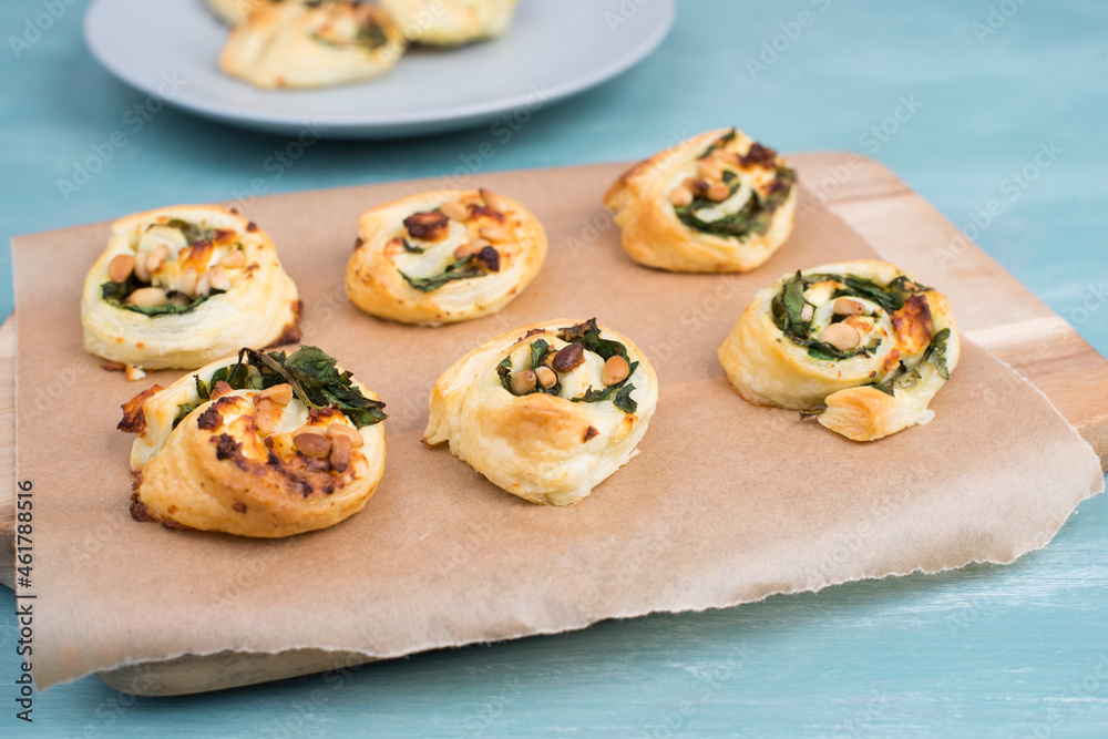 Puff pastry with spinach and feta cheese, rolled up to spirals, fresh from the oven, blue background