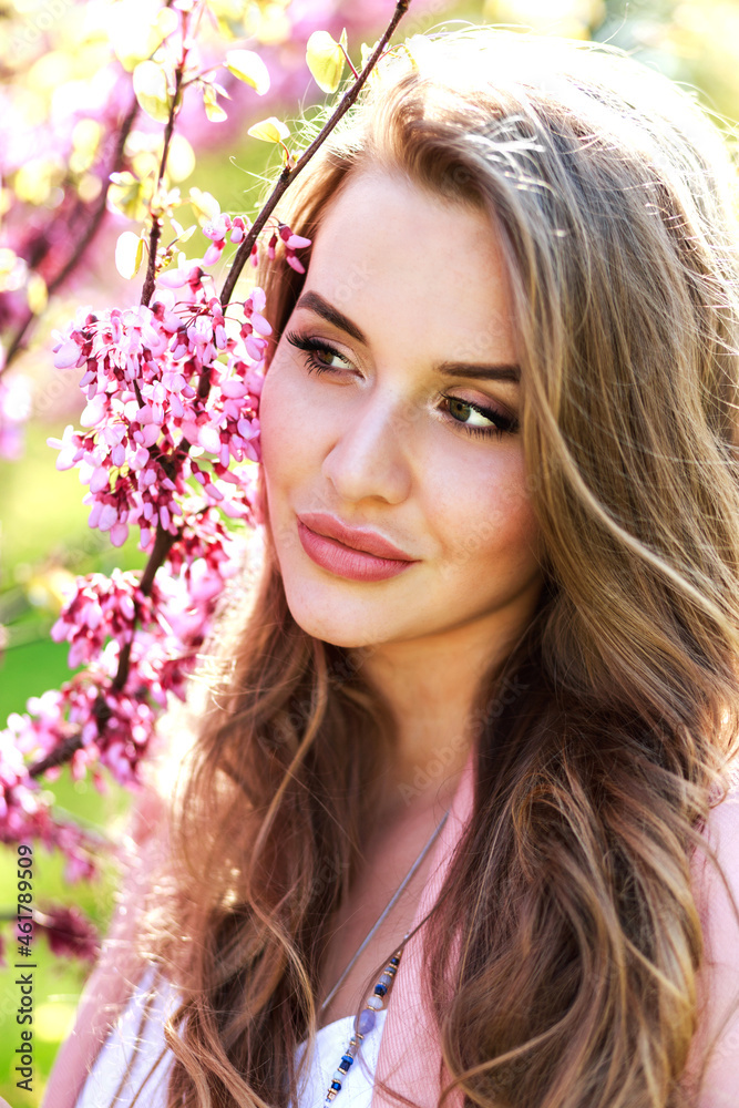 Attractive pretty young woman in light white dress, pink coat, with long hair walking in garden of spring time. Attractive pretty young woman in light white dress, pink coat, with long hair walking in garden of spring time.