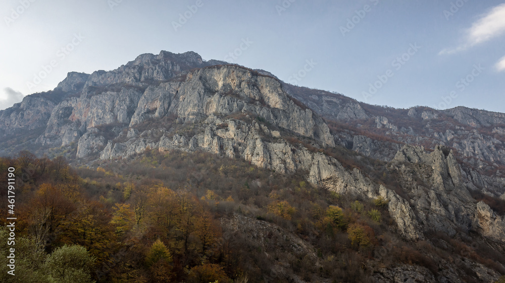 Rocky cliff, autumn colored trees and blue sky above canyon of Jerma river in Serbia
