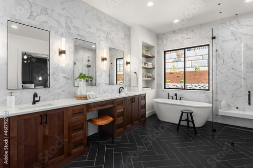 Gorgeous ensuite bathroom in luxury home. Features black herringbone tile floor, marble tile backsplash and wall,  freestanding soaker bathtub, double vanity and sconce lights.