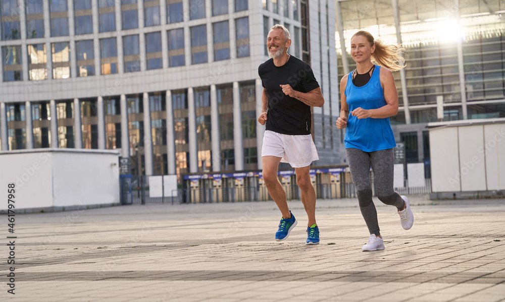Φωτογραφία Mature couple, man and woman exercising and jogging together in the city on a wa