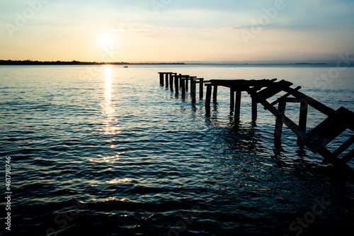 An old wooden walkway leads into the lake with its boards broken and worn by time.