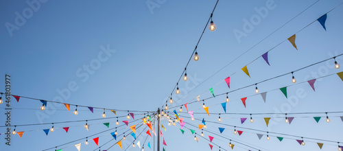 Obraz na płótnie Garland with colorful pennants and light bulbs on pole over blue sky w salonie
