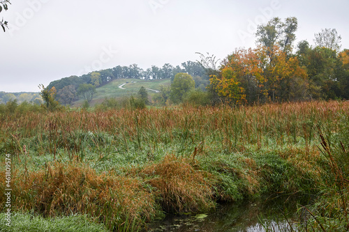 A foggy morning with a river running through a wildflower meadow with a hilly golf course in the background