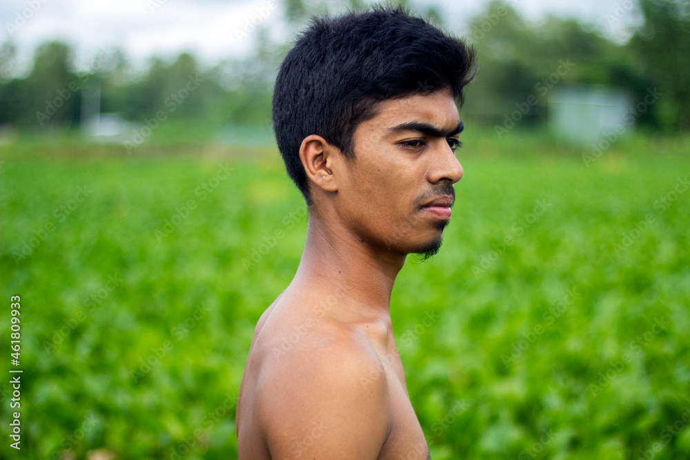A handsome boy is standing in naked the middle of the green nature and has a small beard on his face. the background blur. A handsome boy is standing in naked the middle of the green nature and has a small beard on his face. the background blur.