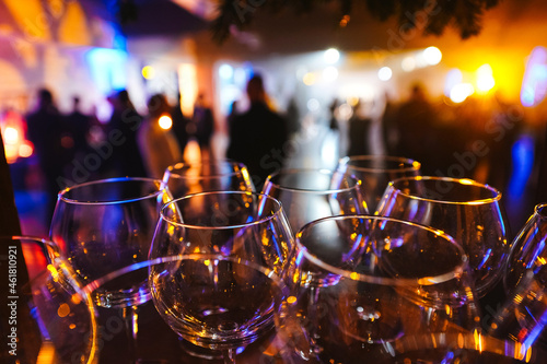 Wine glasses in the light of multicolored lights against the background of blurred silhouettes of people. Large-scale party or private event with catering services