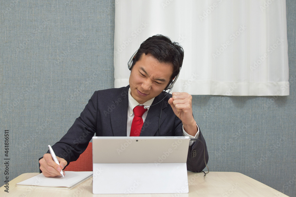 A young Asian man with a headset wearing business suit is in a trouble with customers and gets very angry during telework at home A young Asian man with a headset wearing business suit is in a trouble with customers and gets very angry during telework at home