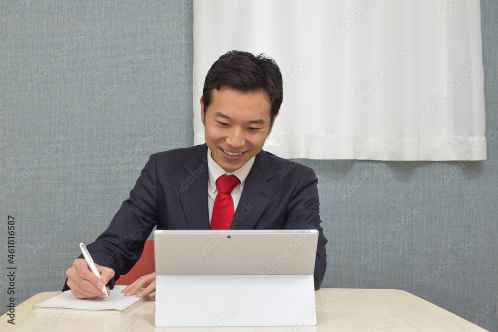 A young Asian man wearng business suit during telework at home takes a memo on a notebook A young Asian man wearng business suit during telework at home takes a memo on a notebook