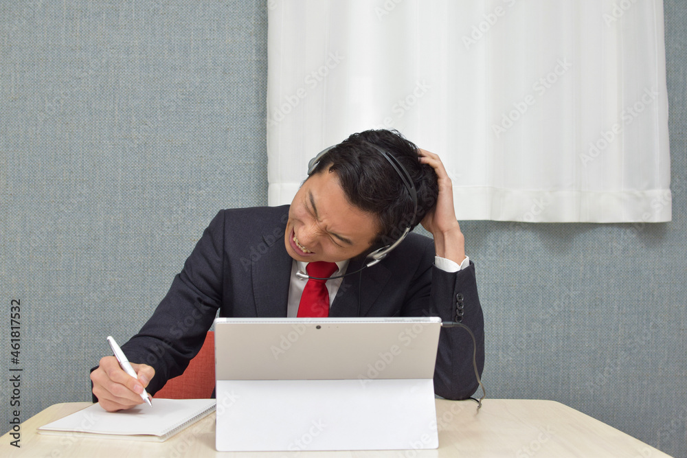 A young Asian man with a headset wearing business suit is in a trouble with customers and gets very angry during telework at home A young Asian man with a headset wearing business suit is in a trouble with customers and gets very angry during telework at home