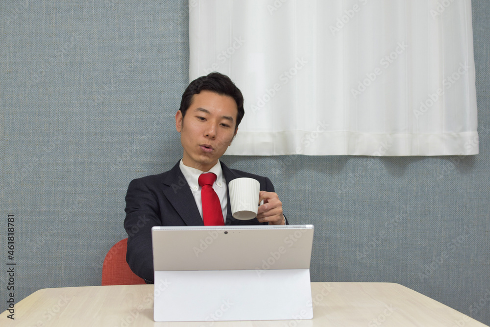 A young Asian man wearing business suit during telework at home takes a rest and drinks a cup of tea/coffee A young Asian man wearing business suit during telework at home takes a rest and drinks a cup of tea/coffee