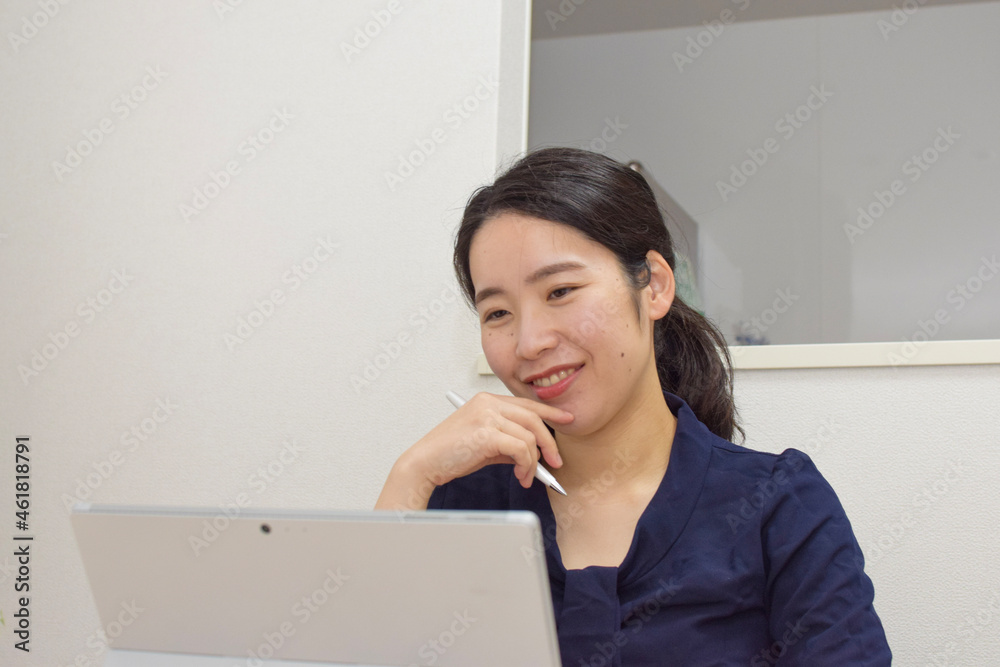 A young Asian woman works at home as telework and smiles at her pc during a meeting A young Asian woman works at home as telework and smiles at her pc during a meeting
