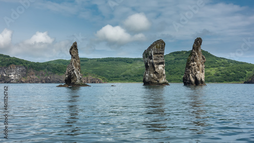 High picturesque cliffs rise above the ocean. Bird nests on steep slopes. Kamchatka coast against the sky and clouds. Rocks Three Brothers. Avacha Bay.