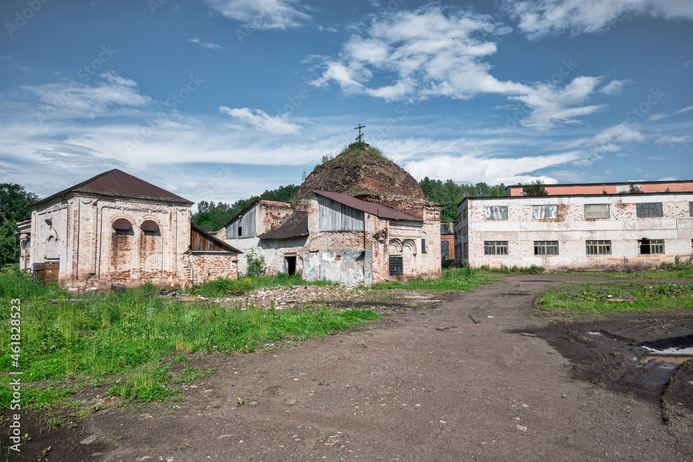 A ruined orthodox church of brick against the trees and blue sky and thin white clouds and road leading to it. Formerly used as warehouse space. Debris scattered all around.