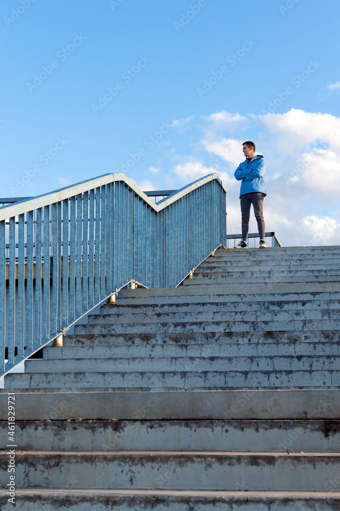 A young sports guy stands at the top of the observation deck and looks into the distance. The concept of overcoming difficulties, climbing to the top. Vertical view.