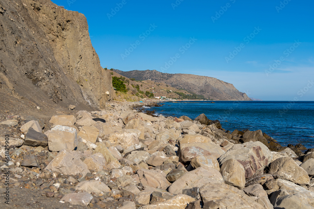 Crimea beach with a rock and large stones near the sea and a small tourist town on the background