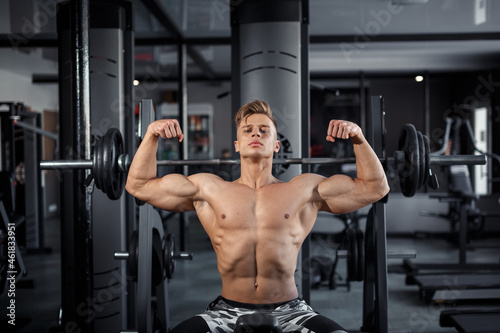 Close Up of a muscular young man lifting weights in gym on dark background. High quality photo