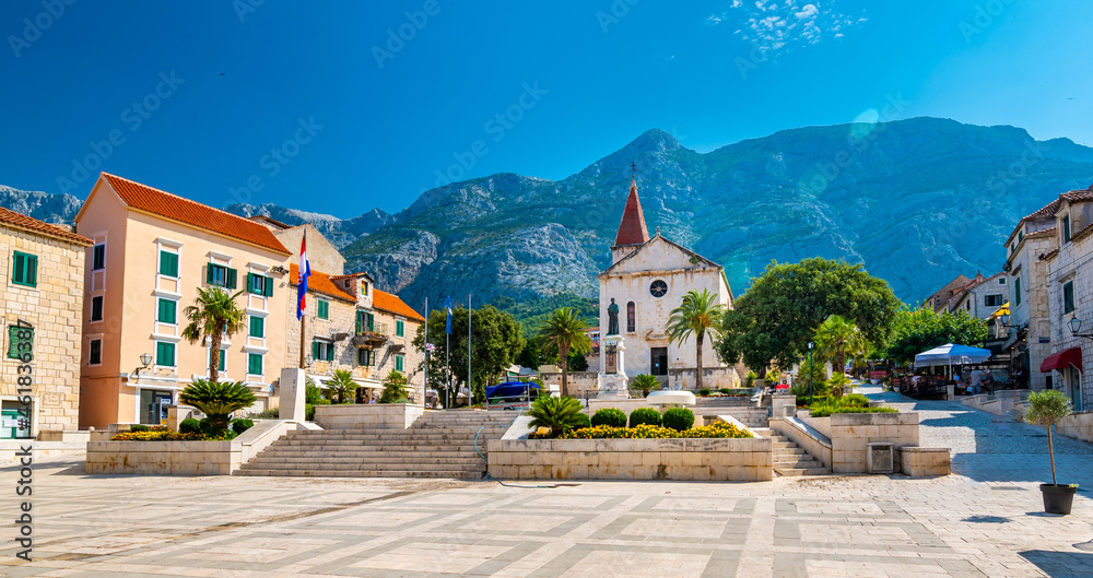Saint Marko cathedral and church at Makarska city, Croatia. The Biokovo mountains in the background. Sunny day at summer, green trees on the side. Dalmatia region.