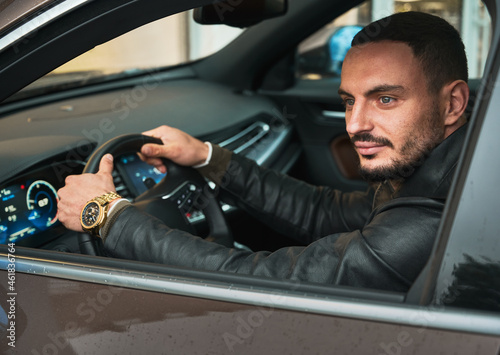 Handsome young man driving modern car, sitting inside.Guy driver wearing casual clothes and gold watch. © anatoliy_gleb