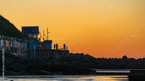Sunset on a harbor scene with silhouettes of people taking photos