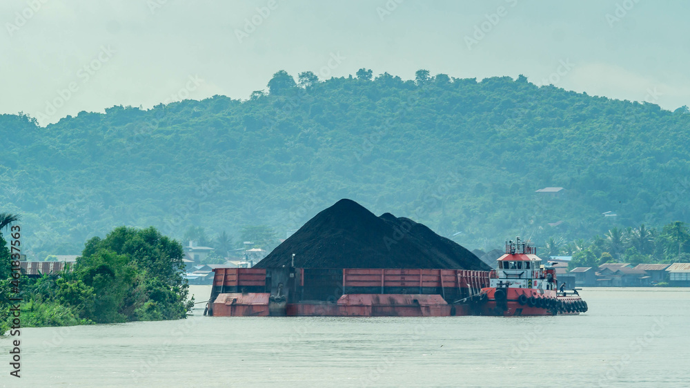 Timber loaded into big barge then drag by a tugboat cruising Mahakam River, Borneo, Indonesia