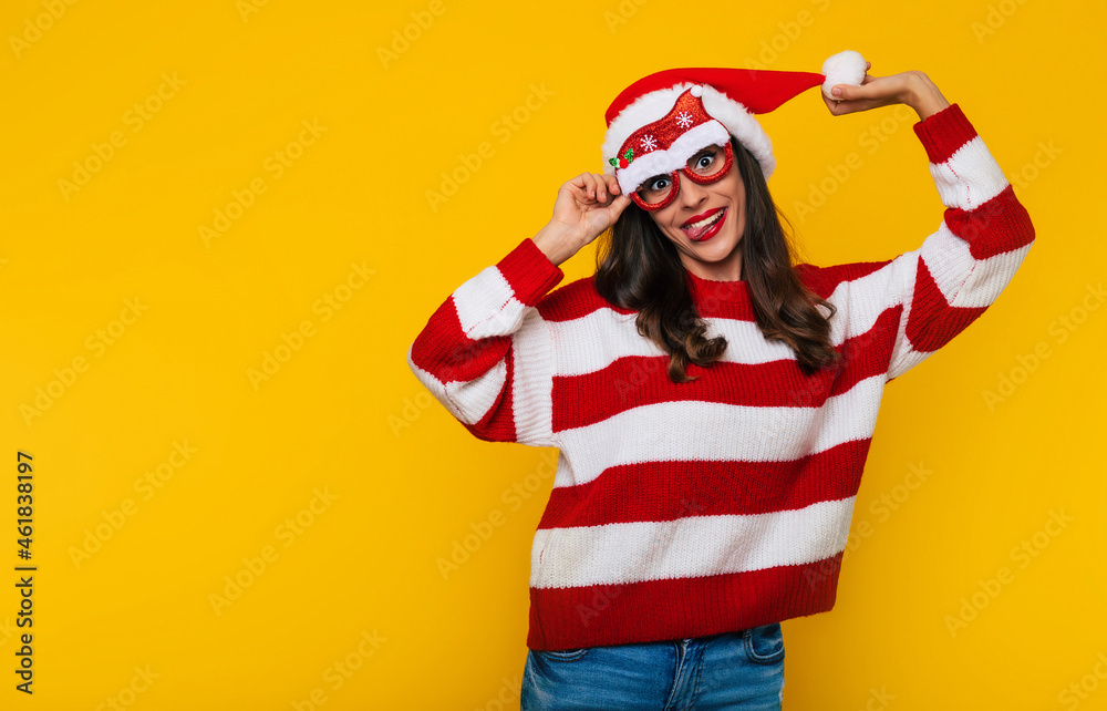 Excited beautiful young woman in funny Christmas glasses and Santa hat is having fun while posing against a yellow wall Excited beautiful young woman in funny Christmas glasses and Santa hat is having fun while posing against a yellow wall